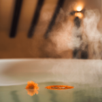 a bathtub filled with warm water, a single calendula flower floating on the surface, steam rising, soft warm lighting